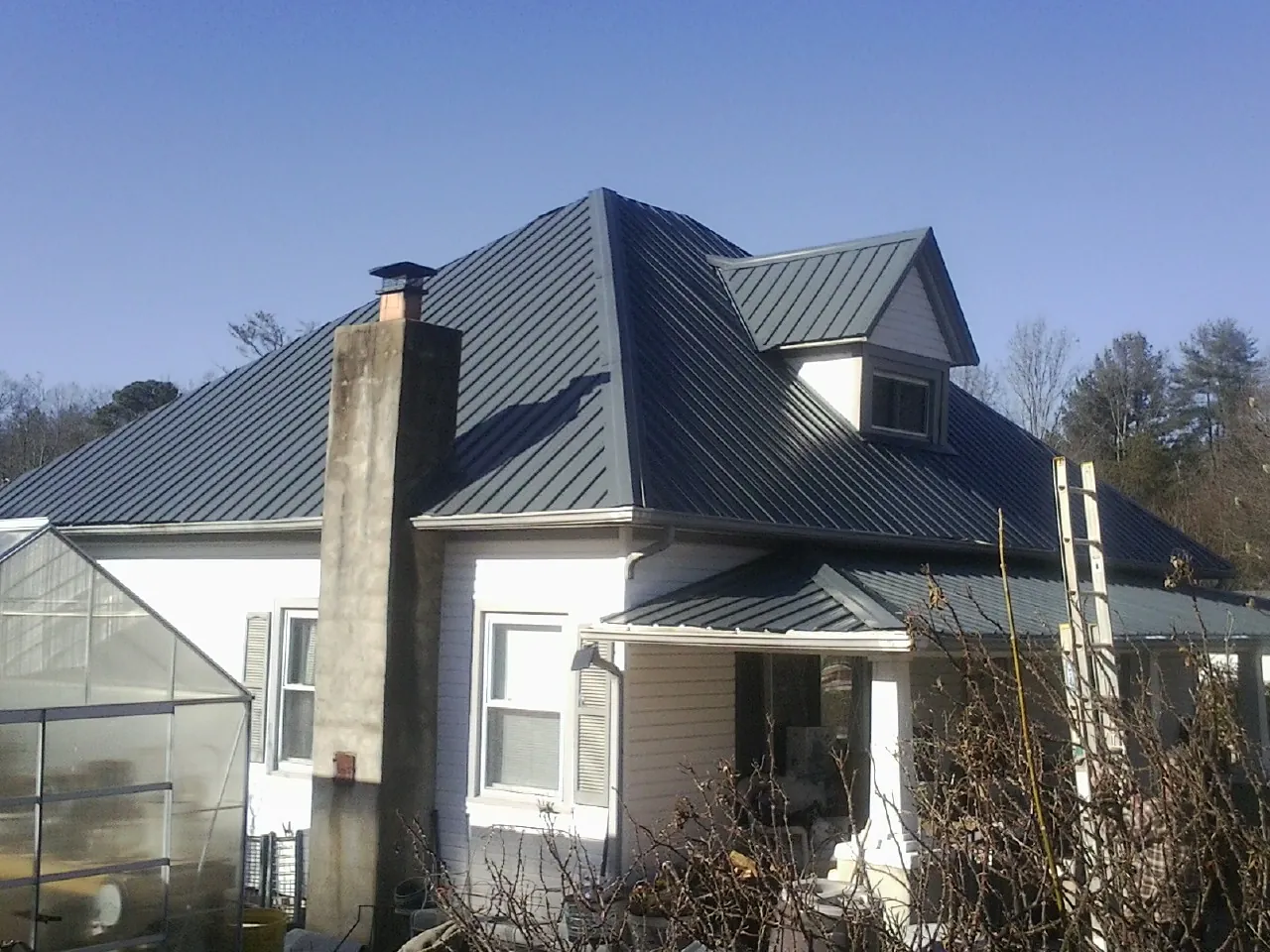 Dark blue standing seam metal roof on a white farmhouse with dormer — Slate & Tile Roof Repair by Roofing Brothers in Locust Valley