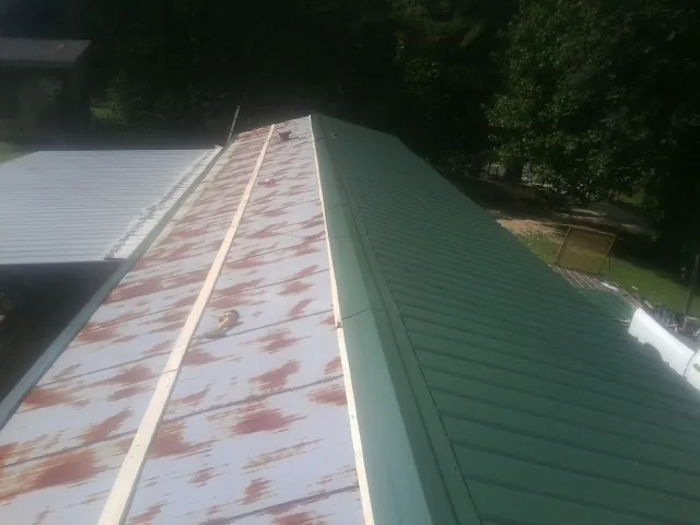 Old rusted panels beside newly installed green metal roofing — Wind Damage Roof Repair by Roofing Brothers in Locust Valley