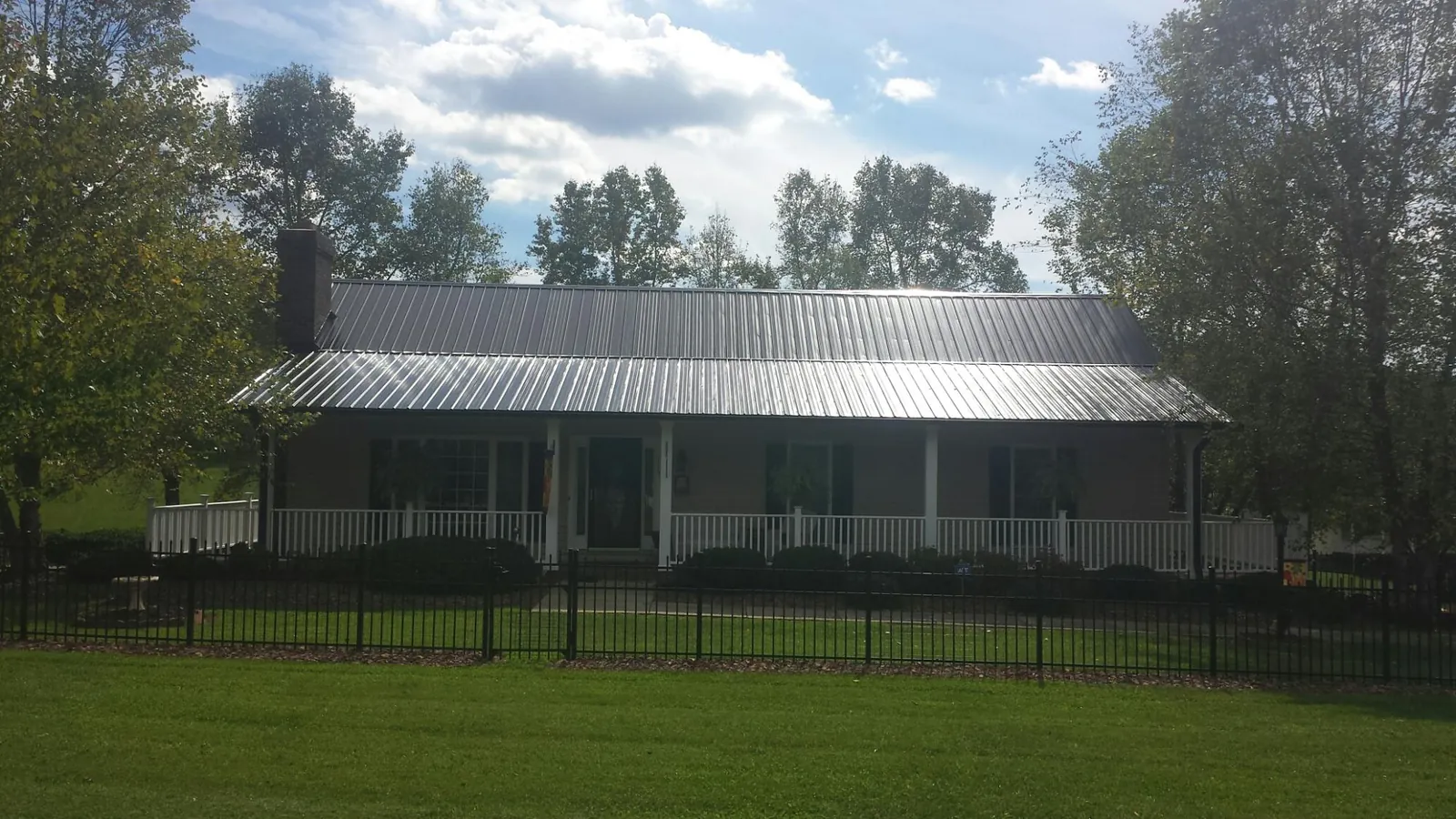 Gray metal roof on a brick ranch with a full width front porch — Gutter Guard Installation work by our crew in Locust Valley