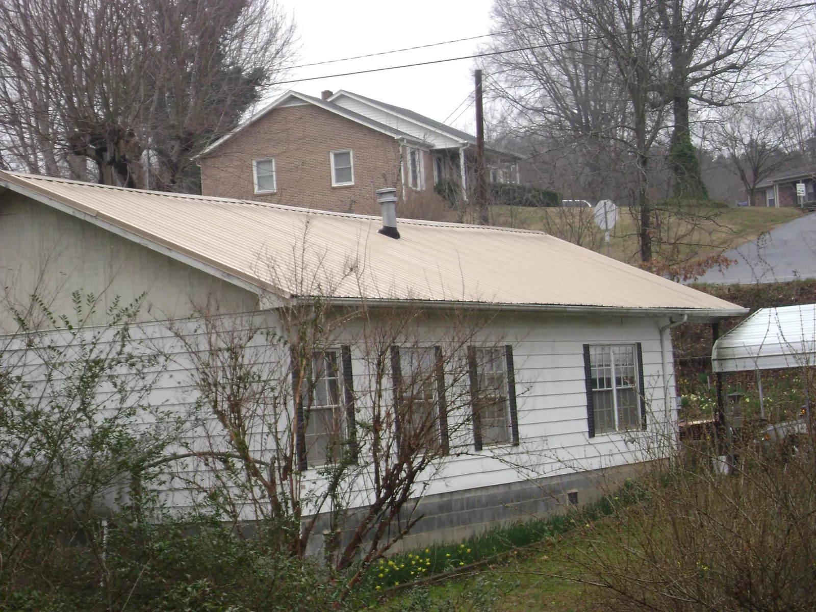 Tan metal roof on a white sided house set into a hillside — Commercial Roofing by Roofing Brothers in Locust Valley