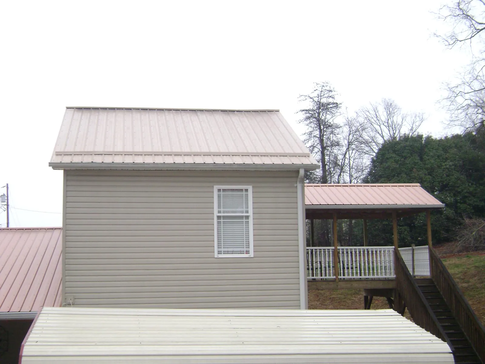 Tan metal roofs on a two story addition and attached porch, from a Roof Replacement job in Locust Valley