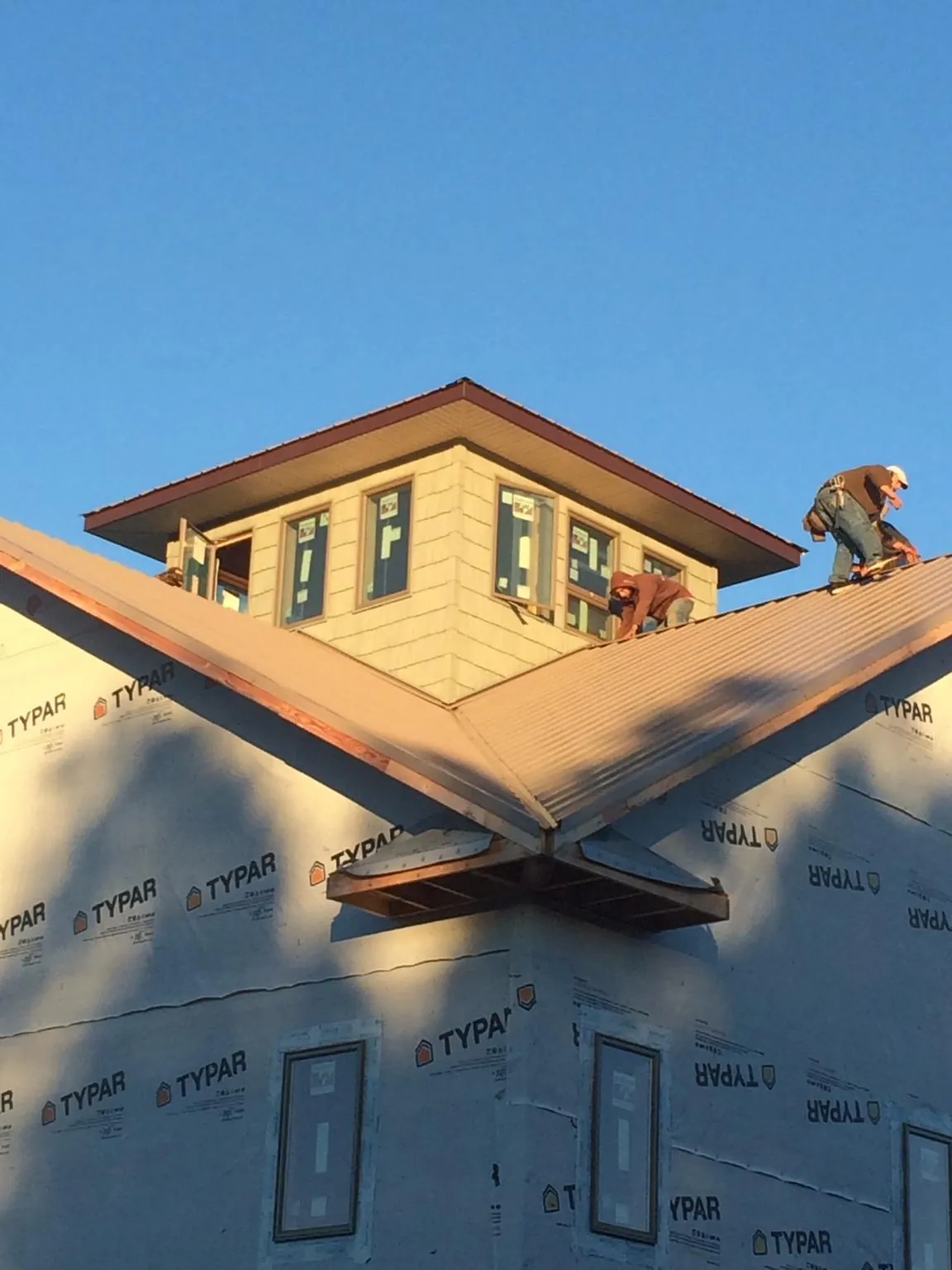 Roofers working around a rooftop cupola on a new metal roof at sunset — Roof Waterproofing in Locust Valley by Roofing Brothers